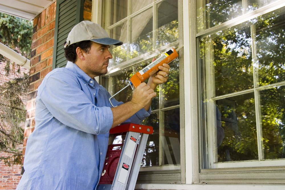 a man sealing and repairing a window with caulking